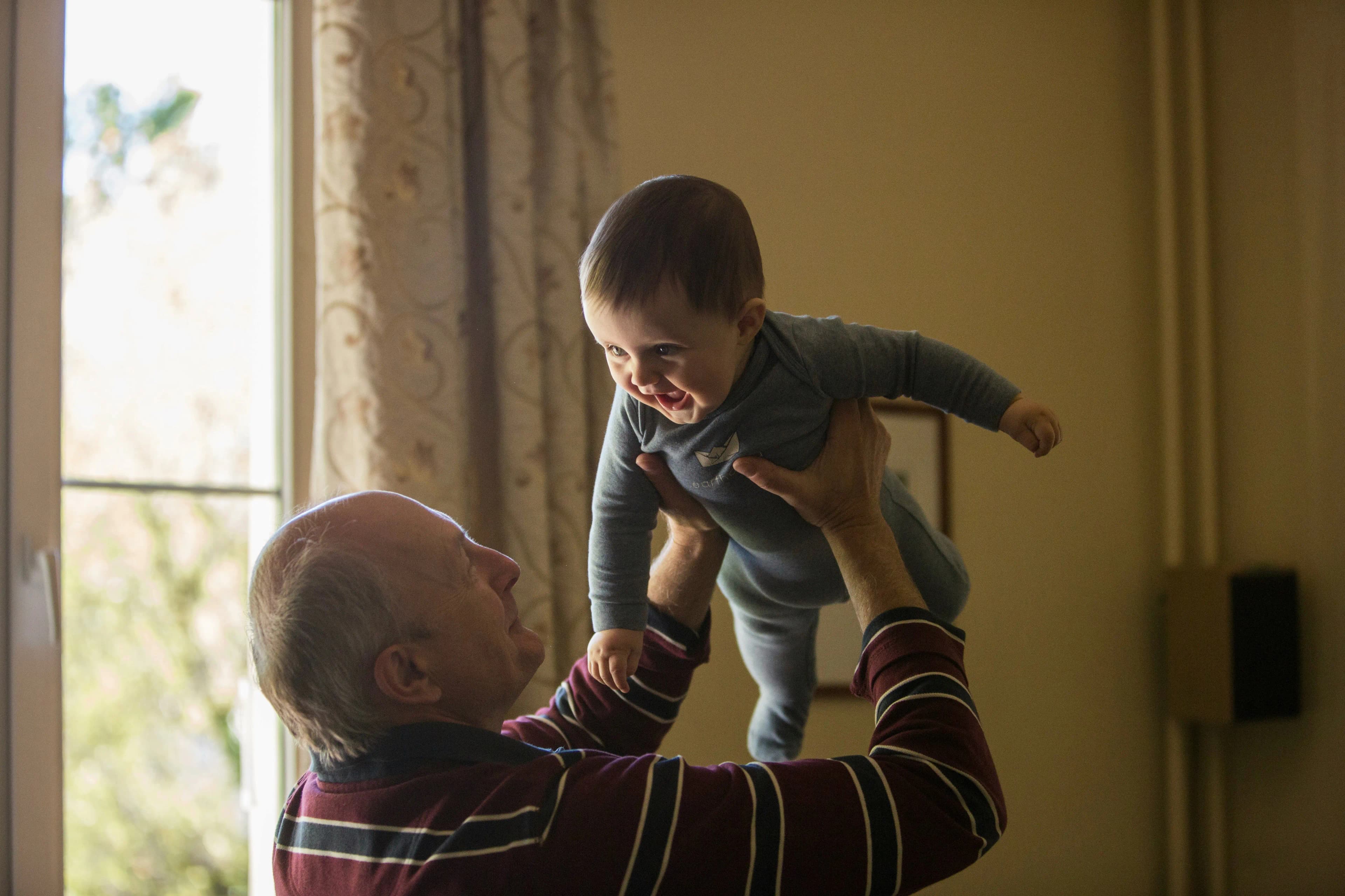 A grandfather lifting his grandchild in a warm indoor family moment